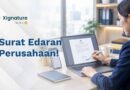 Staf HR menandatangani contoh surat edaran perusahaan secara digital di laptop, dengan ponsel berisi grup chat di sampingnya
